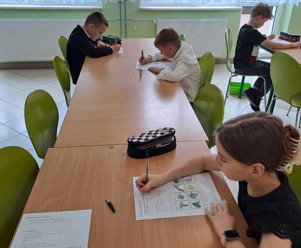 Dzieci, które siedzą przy ławkach i piszą test o lesie.