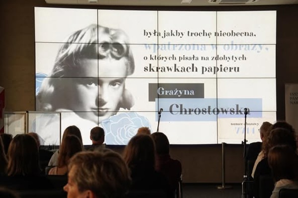 na ekranie wyświetlony jest portret Grażyny Chrostowskiej, uczestnicy konferencji siedzą na widowni