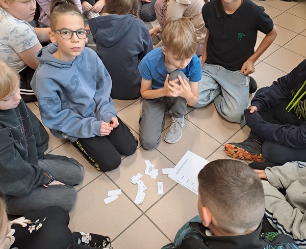 Dzieci siedzące na podłodze, na której leżą karteczki.