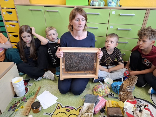 Dzieci siedzą na dywanie, prowadząca prezentuje żywy ul.