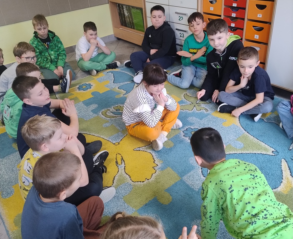 grupka dzieci siedząca w okręgu a jedna dziewczynka w środku