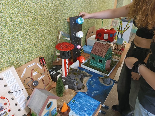 dziewczynka dotyka ręką układu planet, obok kolorowe domki