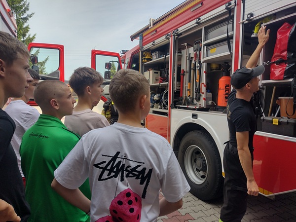 Grupa uczniów ogląda wyposażenie wozu strażackiego.