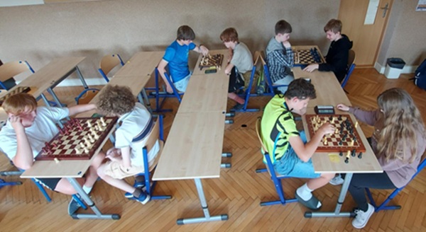 cztery pary uczniów siedzi przy stolikach i rozgrywa partię szachów.