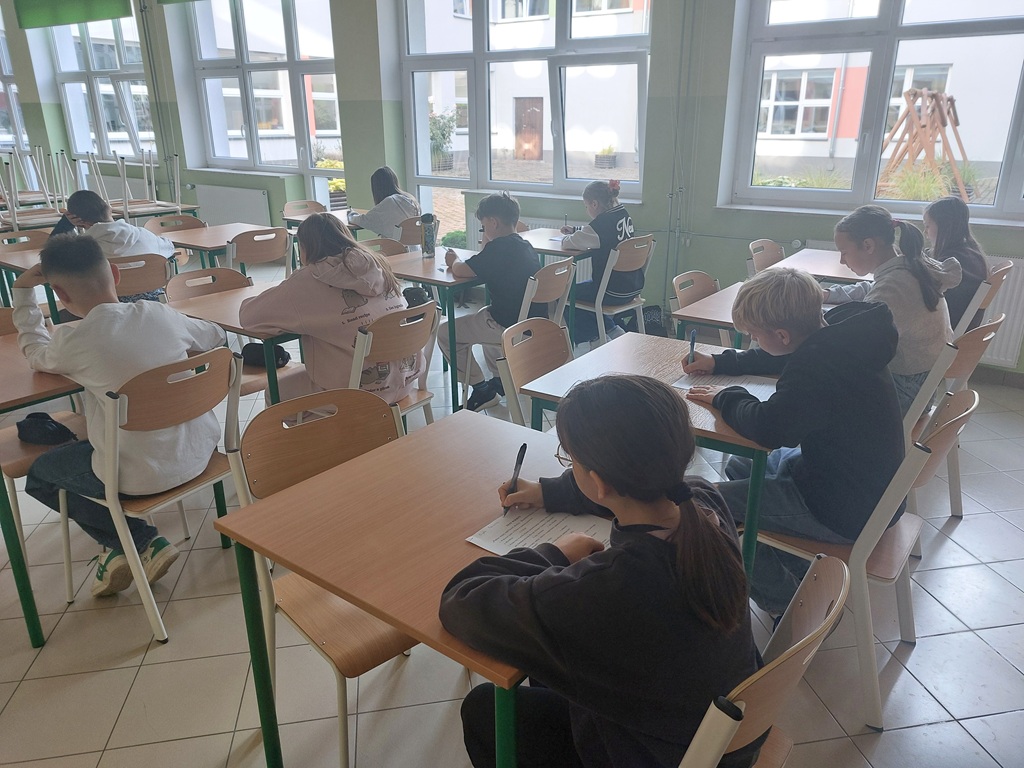 Uczniowie ze skupieniem piszący test wiedzy. W tle sala konkursowa.