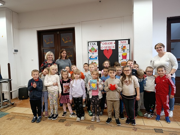 uśmiechnięte dzieci i 3 panie stoją na tle tablicy jak dbać o serce