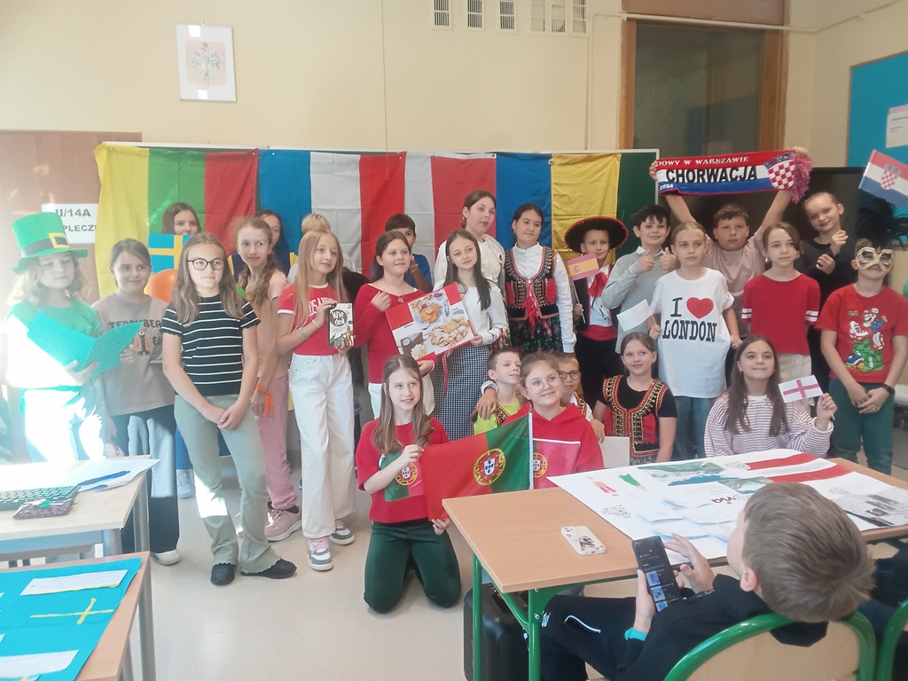 Uśmiechnięta grupa uczniów w barwnych strojach uczestniczących w wydarzeniu, trzymają flagi i plakaty