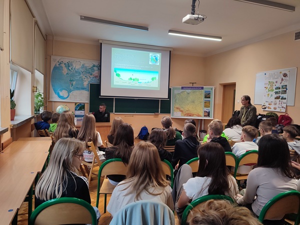 Sala lekcyjna z uczniami i dwoma mężczyznami na warsztatach.