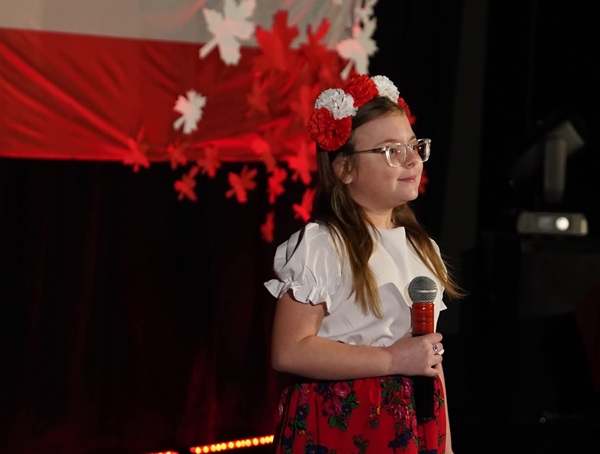 dziewczynka w biało czerwonym stroju, trzymająca mikrofon