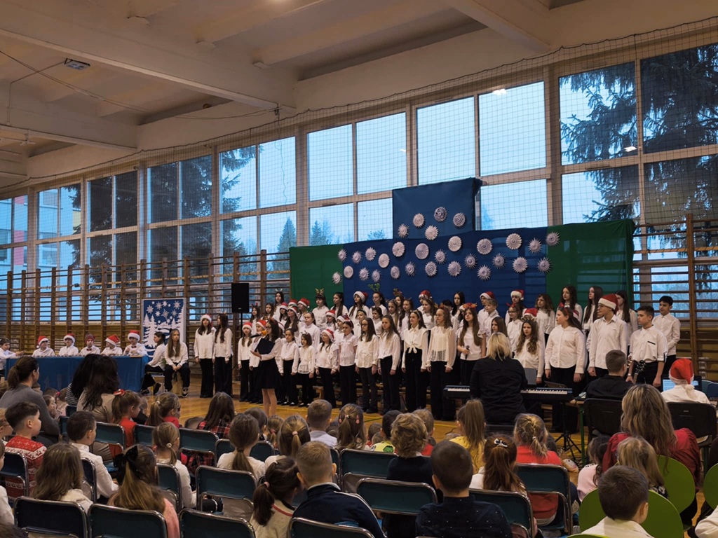 Szkolny chór stoi na tle świątecznej scenografii w budynku przy ulicy Szkolnej 53.