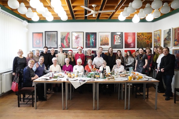 Uczestnicy spotkania pozują do zdjęcia za stołem wigilijnym.