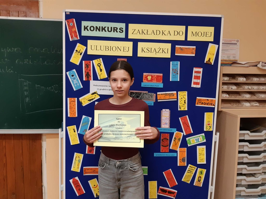 laureatka 1 miejsca prezentuje dyplom na tle tablicy z pracami