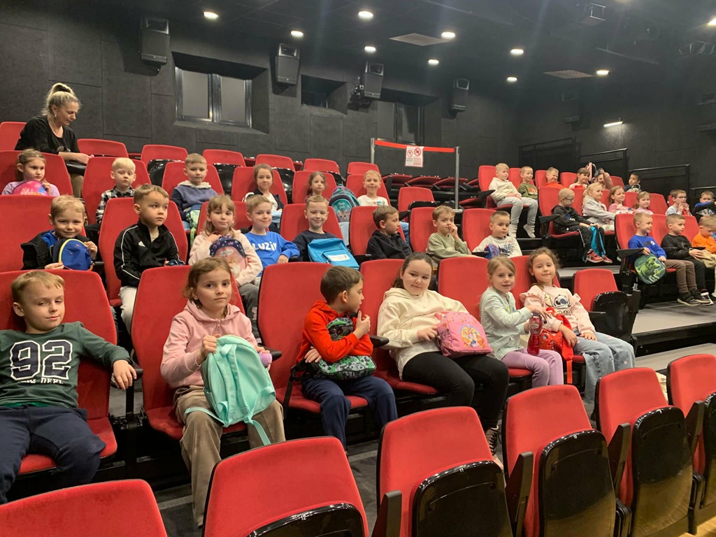 Dzieci z grupy 0 B z uśmiechem siedzą w sali kinowej i oglądają bajkę
