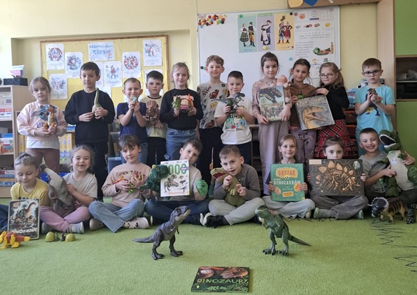 dzieci robią miny groźnych dinozaurów, trzymają w dłoniach książki, maskotki, figurki dinozaurów.