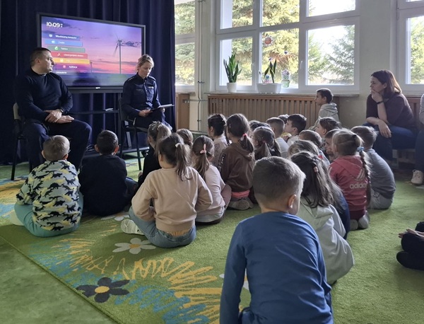 dzieci siedzące na dywanie oraz funkcjonariusze policji.