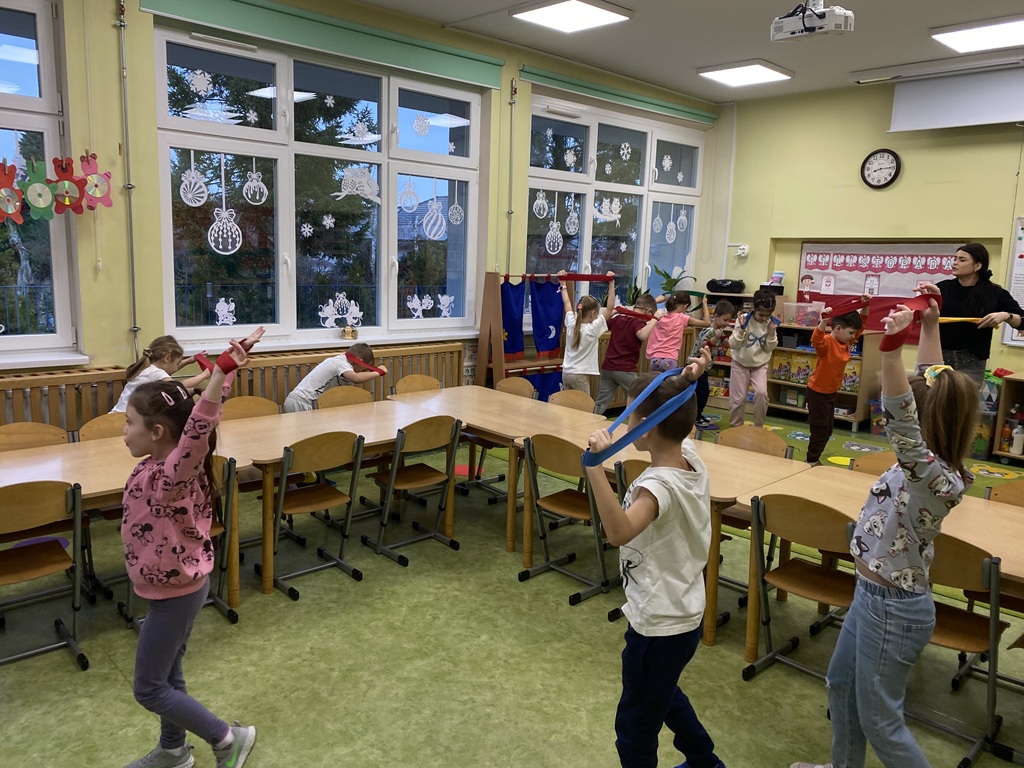 Dzieci z szarfami uniesionymi na wyprostowanych rękach nad głową