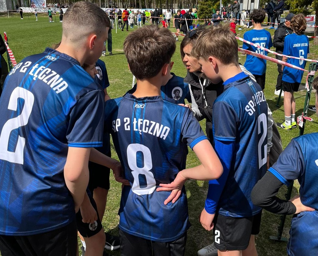 chłopcy stoją razem na boisku czekają na bieg i słuchają wskazówek nauczyciela.