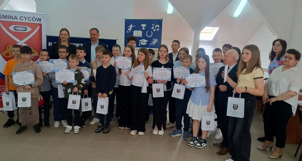 uśmiechnięte dzieci, stoją i trzymają w dłoniach dyplomy i torby z prezentami.