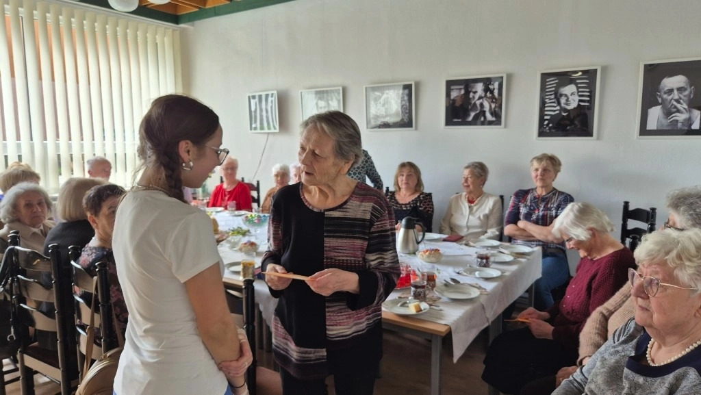 spotkanie wielkanocne z Klubem 50 PLUS: seniorka odbiera życzenia od wolontariuszki