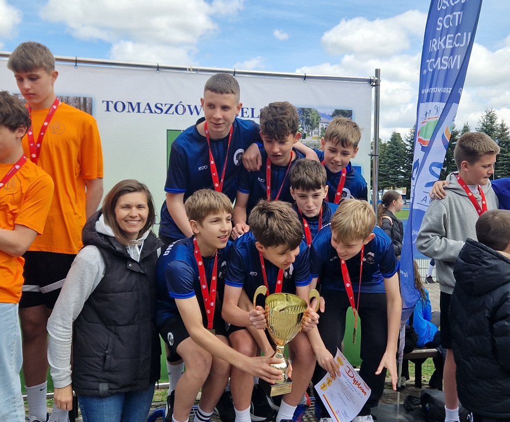 Grupa uczniów z medalami stoi na podium, trzymając puchar i dyplom.