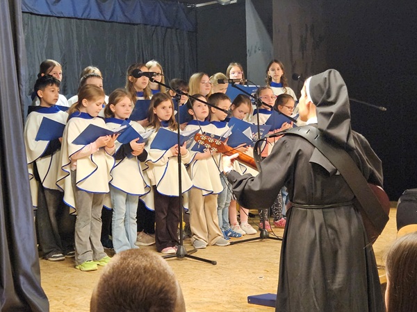 grupa dzieci śpiewa na scenie, siostra zakonna gra na gitarze