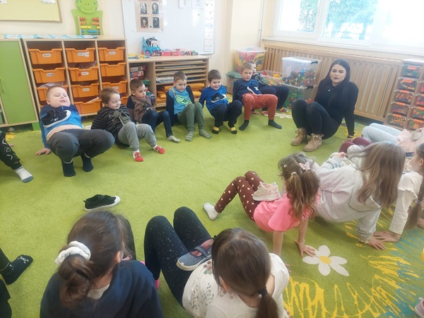 Grupa dzieci ćwiczy w kole na dywanie.