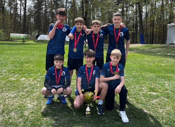 zawodnicy w strojach sportowych stoją na trawie, trzymając medale i puchar.