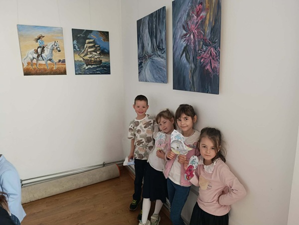 Uśmiechnięte dzieci stoją przy wystawie malarskiej