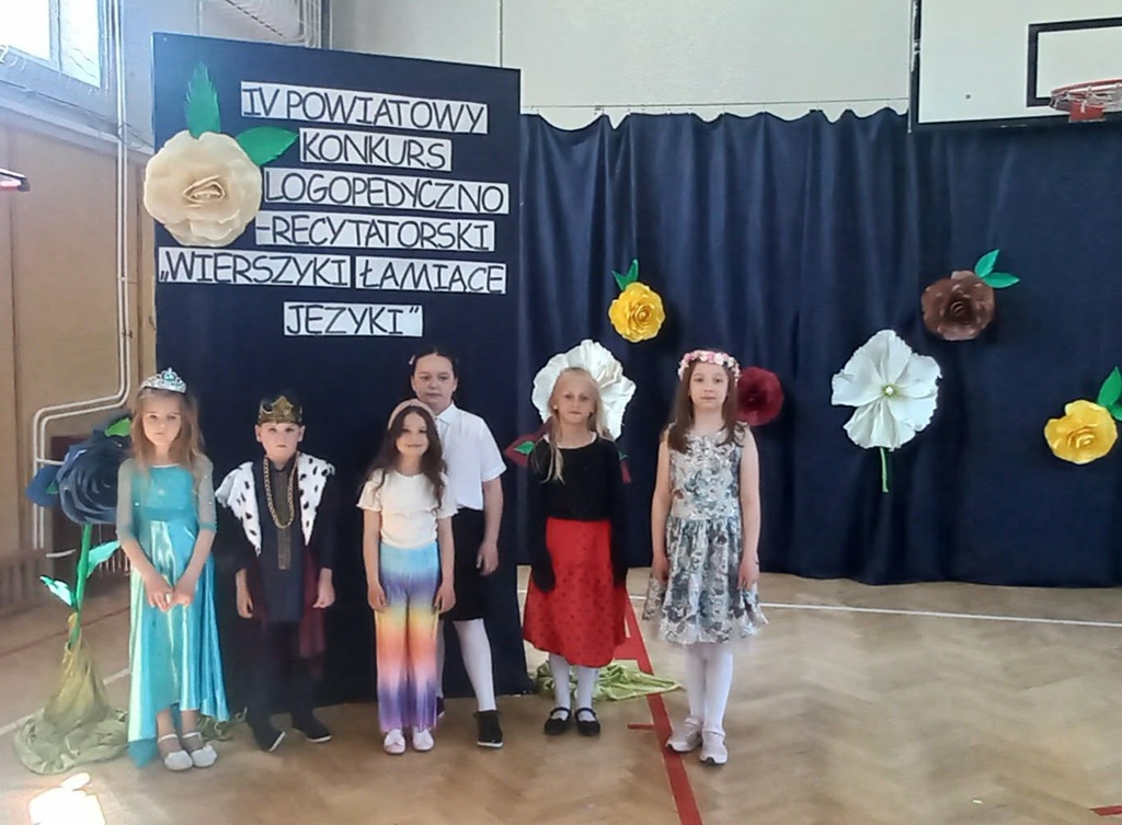 Grupowe zdjęcie uczestników konkursu, w tle napis i papierowe, kolorowe kwiaty.