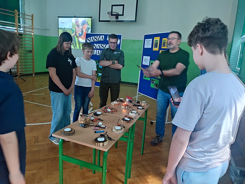 prowadzący spotkanie i uczniowie przy stoliku z różnymi rzeczami