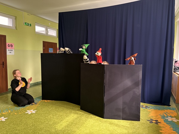 Na dywanie prowadząca zajęcia teatralne. Za parawanem dzieci z pacynkami