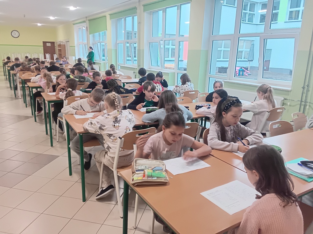 grupa uczniów reprezentujących klasy 2 i 3, piszących test na stołówce szkolnej.