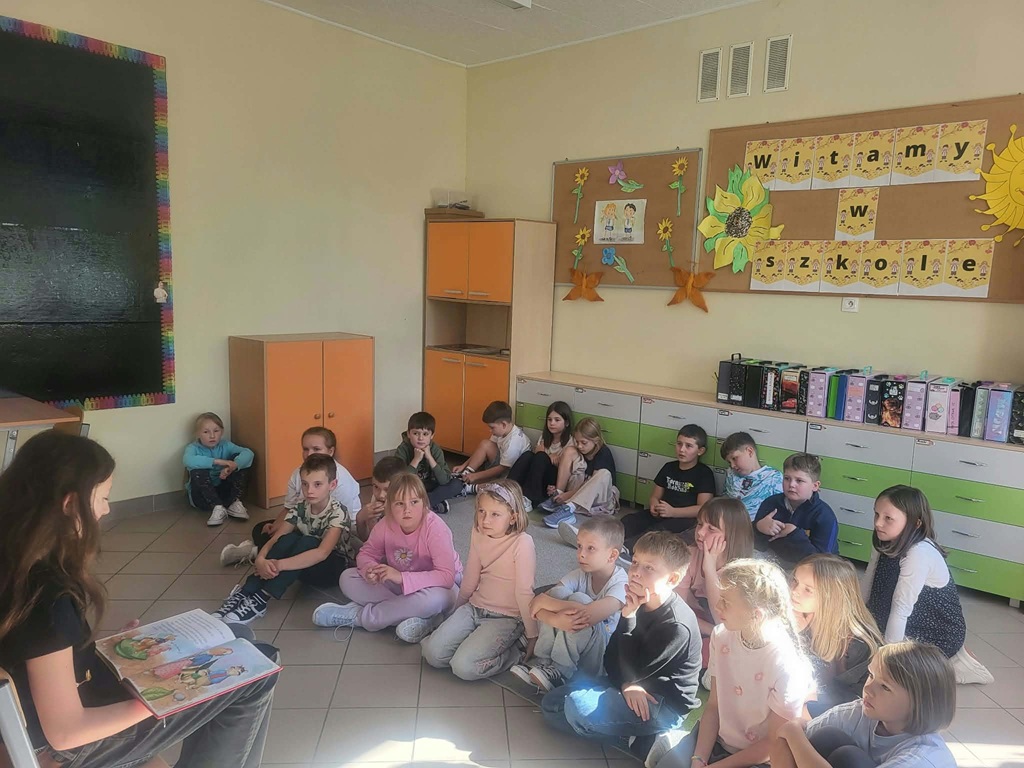uczniowie słuchają czytania starszej koleżanki.
