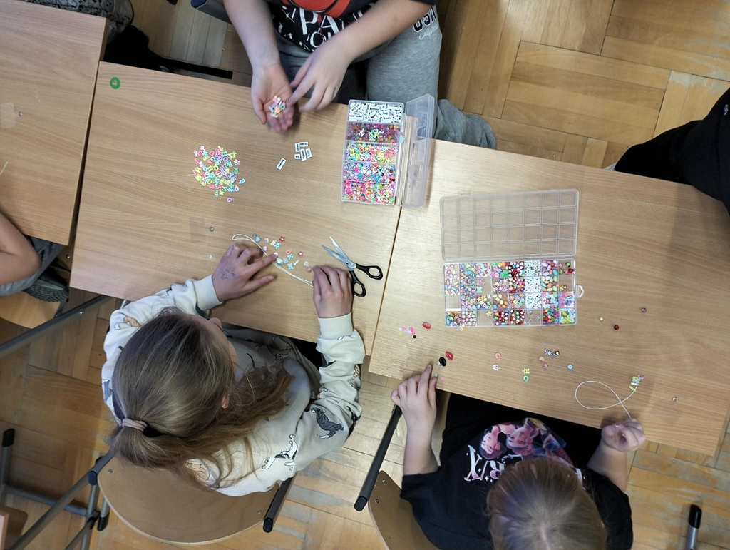 Dziewczynki siedzą przy stolikach robiąc zawieszki z koralików.