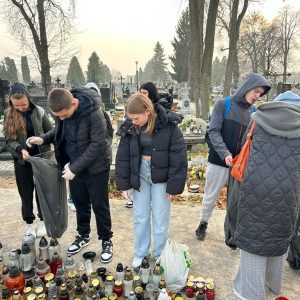 uczniowie i nauczycielki zbierają wypalone znicze przy grobie żołnierzy.