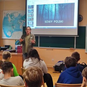 Sala lekcyjna z uczniami siedzącymi na krzesełkach na warsztatach. Na środku sali stoi mężczyzna.