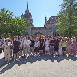 Duża grupa uczniów stoi na tle drzew i zamku