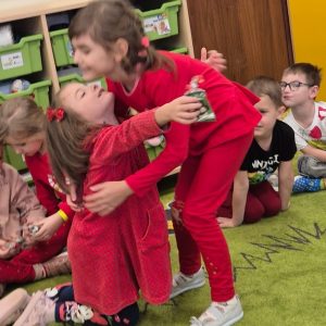 Dwie dziewczynki siedzą na dywanie, przytulają się i trzymają w rękach prezenty od Mikołaja.