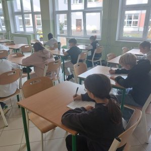 Uczniowie ze skupieniem piszący test wiedzy. W tle sala konkursowa.