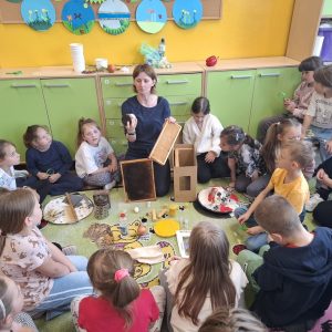 prowadząca warsztaty prezentuje dzieciom akcesoria pszczelarskie