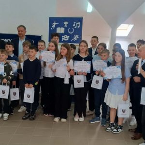 uśmiechnięte dzieci, stoją i trzymają w dłoniach dyplomy i torby z prezentami.