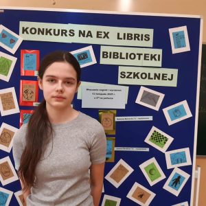 laureatka 1 miejsca prezentuje dyplom na tle tablicy z pracami