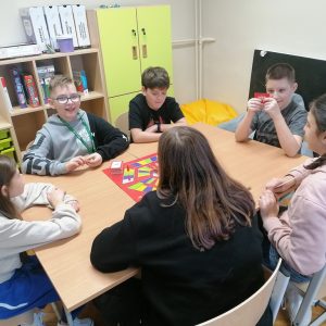 trzech uczniów i trzy uczennice siedzą przy stolikach, grają w grę planszową