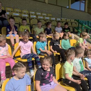 Dzieci siedzą na trybunie stadionu piłkarskiego
