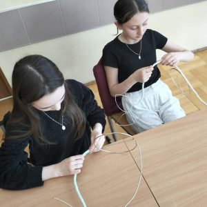 Dziewczynki z kółka w trakcie zajęć nawlekają sznurek dziewiarski na drut.