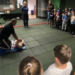 Mężczyzna w klęku przed fantomem, pokazuje masaż serca