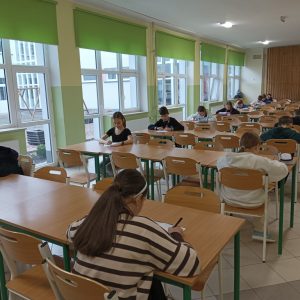 Uczniowie siedzą na dwóch przeciwległych końcach ławek, pochyleni nad kartką papieru.