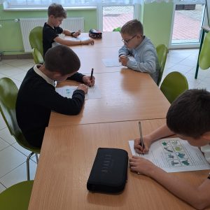 Przedstawia dzieci siedzące przy stole i rozwiązujące test o lesie.
