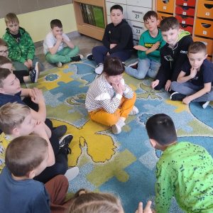 grupka dzieci siedząca w okręgu a jedna dziewczynka w środku