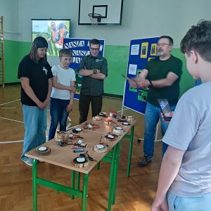 prowadzący spotkanie i uczniowie przy stoliku z różnymi rzeczami